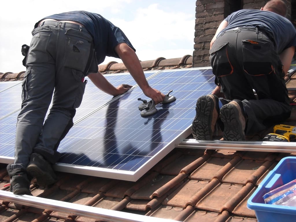 Two installers mounting solar panels on a tile roof